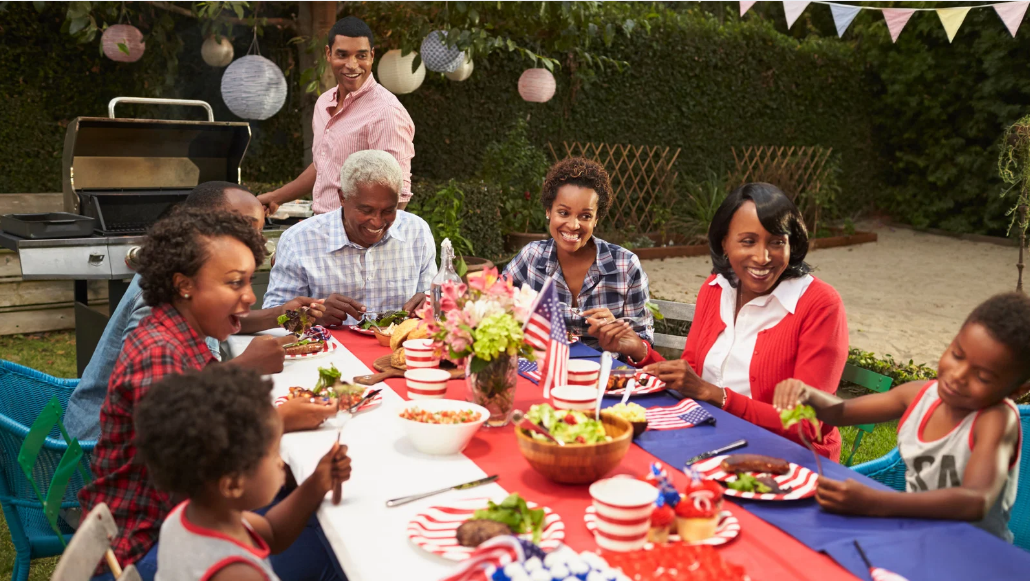 Family safely grilling and eating lunch at a backyard table on Labor Day